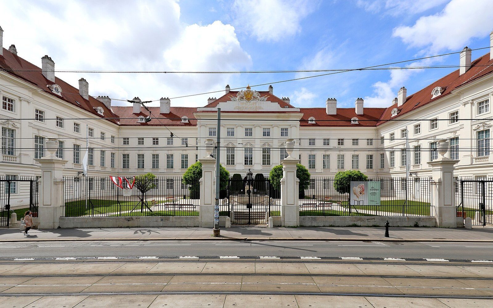 Baroque palace facade with red roof behind wrought-iron gates and a courtyard